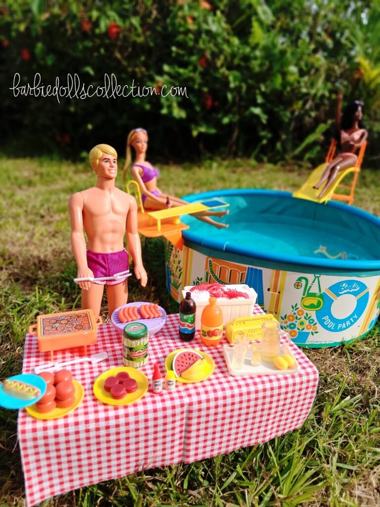 Wide view of the Barbie summer pool party diorama showing a food table filled with party snacks, Ken near the barbecue, and the swimming pool in the background.